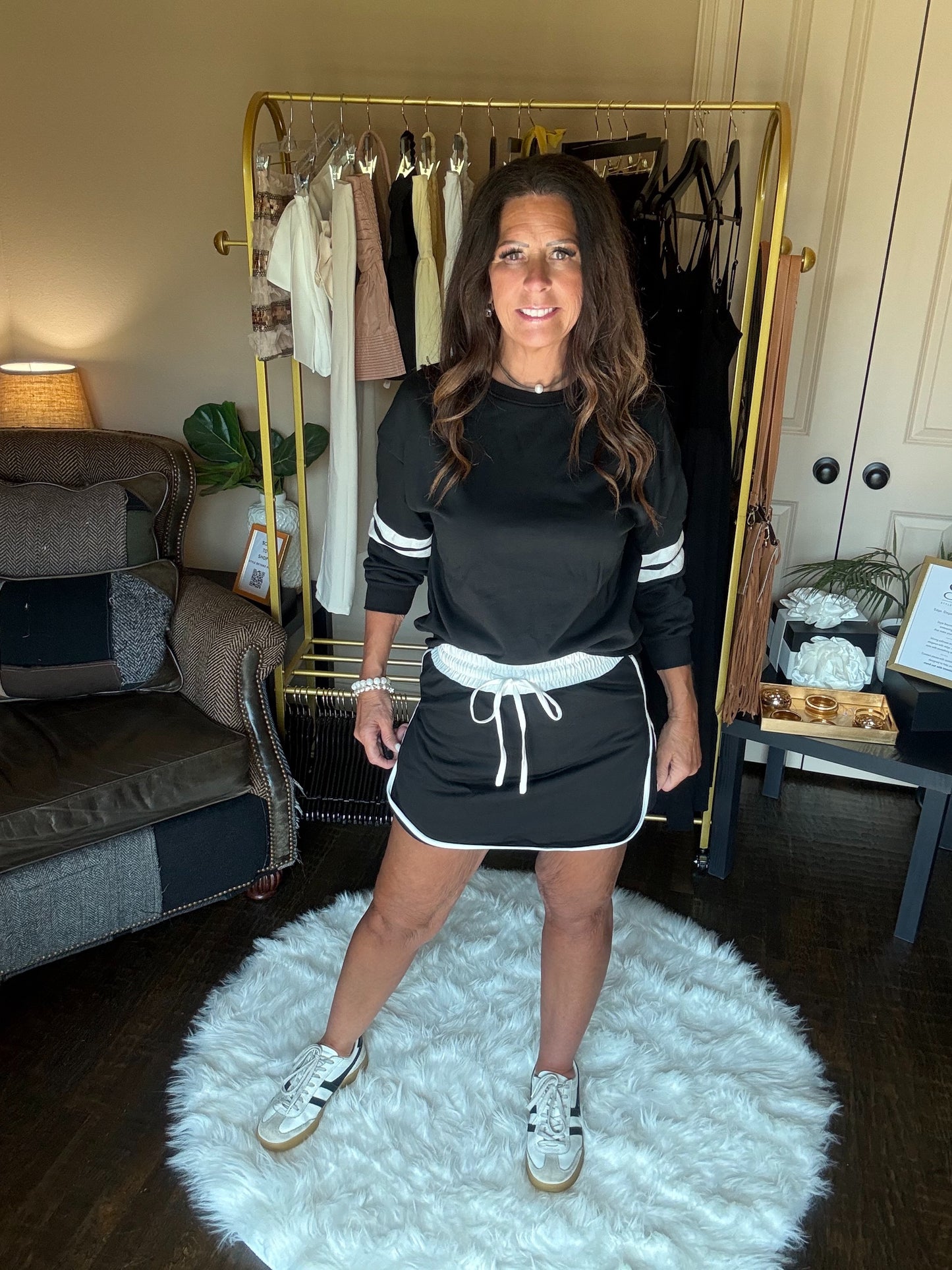 Woman in black and white outfit standing on a white rug in a room with a clothing rack.