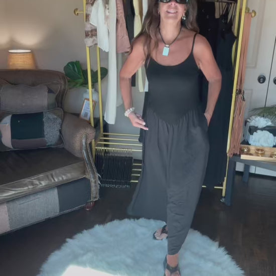 Woman in a black dress and sunglasses standing in a room with a clothing rack and furniture.