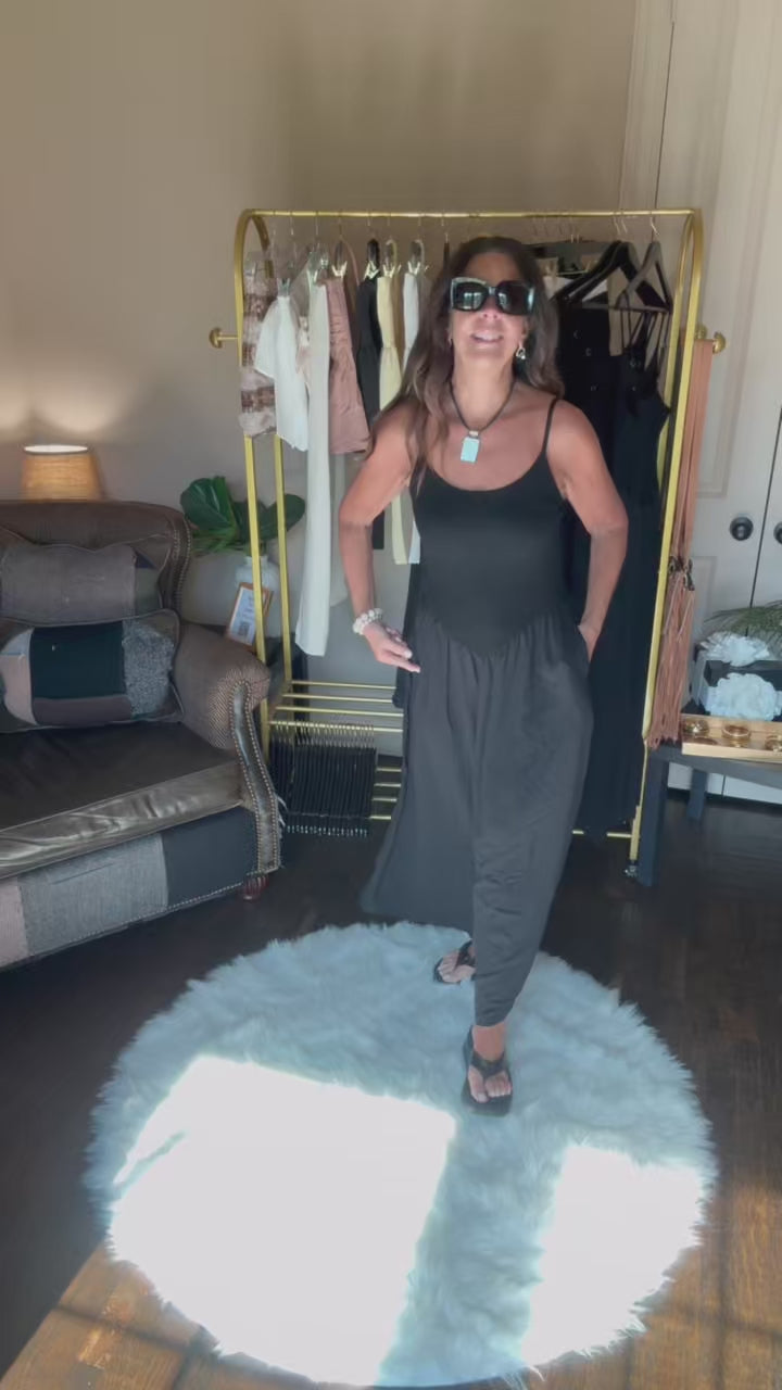 Woman in a black dress and sunglasses standing in a room with a clothing rack and furniture.