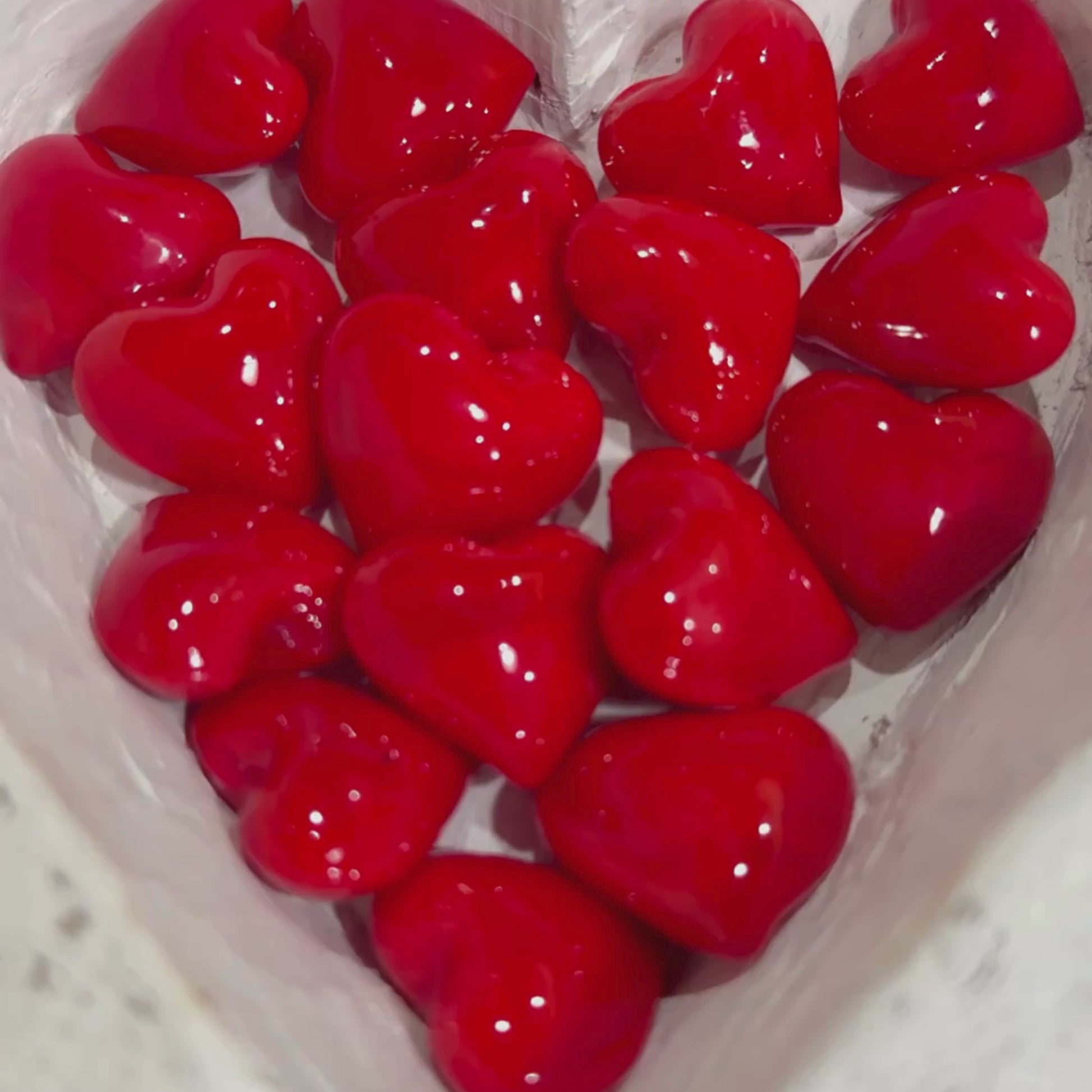 Tiny red glass hearts with a hand picking one up to show size.