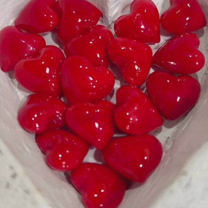 Tiny red glass hearts with a hand picking one up to show size.
