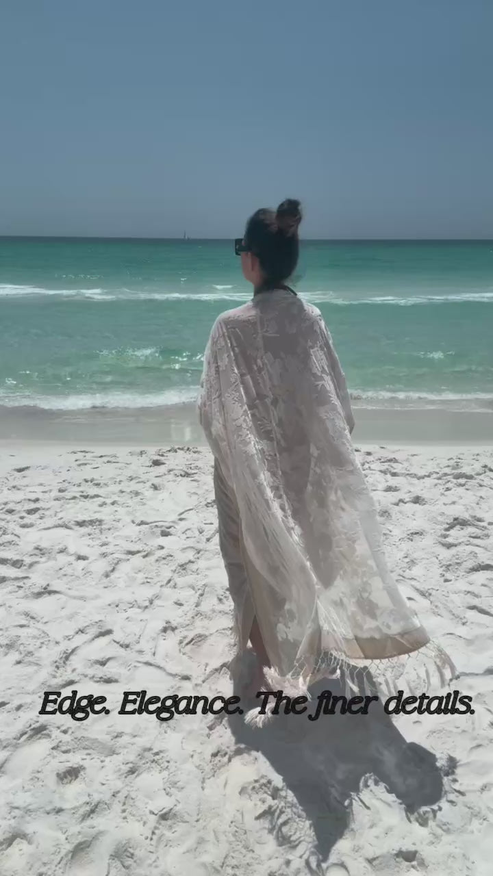Load video: woman modeling ivory kimono on beach with ocean background