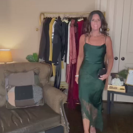 Model is wearing an asymetrical satin dress with delicate lace trim in a rich hunter green color.