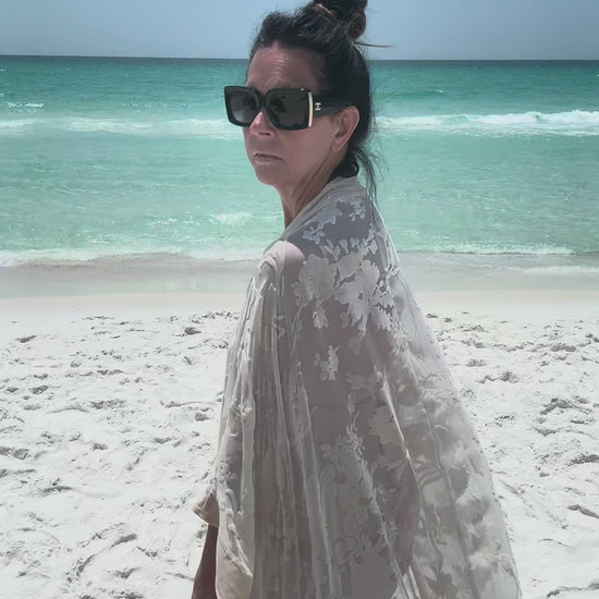 woman walking on beach with ocean background wearing ivory kimono