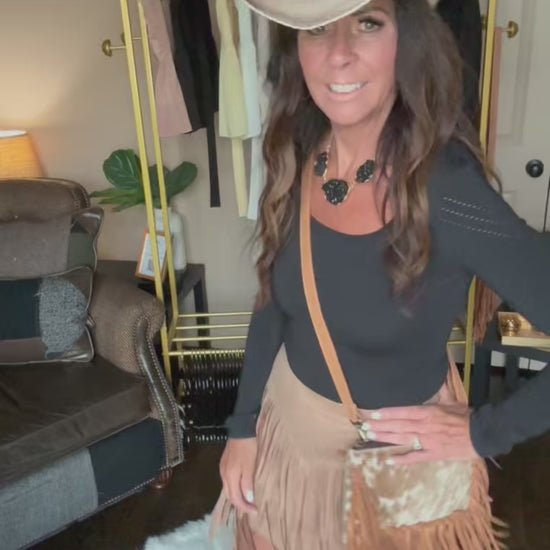 Woman modeling a tan fringe crossbody bag.
