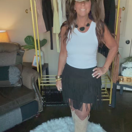 Woman modeling a black fringe midi skirt in a home boutique.